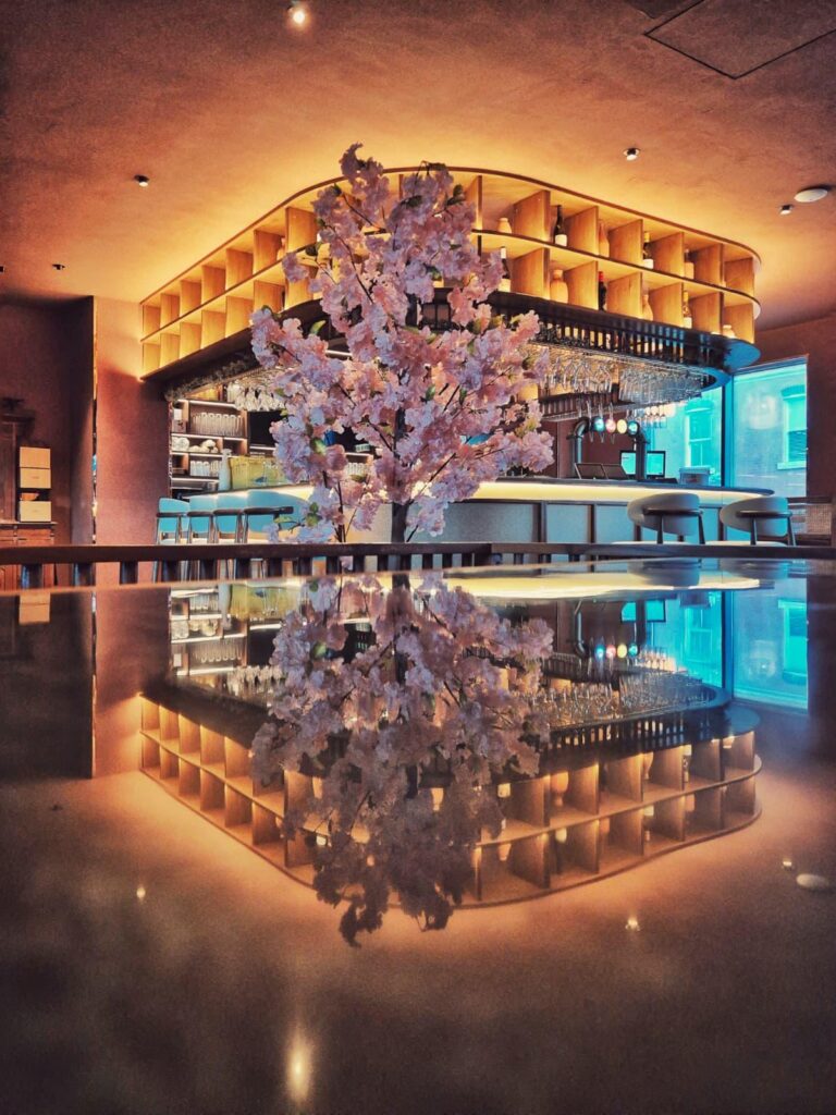 Elegant bar with a central cherry blossom tree and circular shelving above, warm amber lighting.